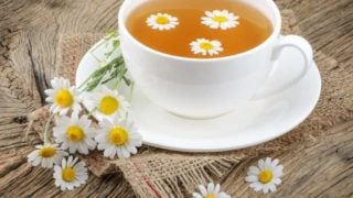 Chamomile tea in a white cup and chamomile flowers on a table