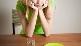 A thin girl looking pensively at half a slice of bread and a glass of water
