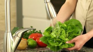 A person cleaning green leafy vegetable under running water