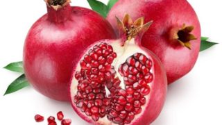 Two fresh pomegranates with a sliced pomegranate on a white background