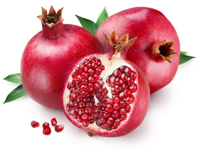 Two fresh pomegranates with a sliced pomegranate on a white background