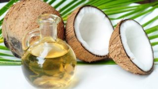 A bottle of coconut oil with coconuts and green palm tree leaves on a white table