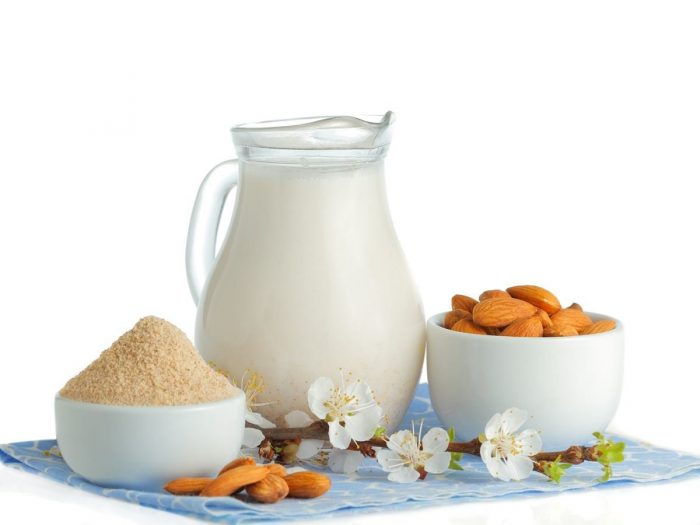 A jug of almond milk, a bowl of almond flour, almond blossoms, and whole nuts