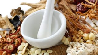 White marble mortar and pestle surrounded by herbs and spices