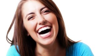 A beautiful young woman in a blue top laughing against a white background
