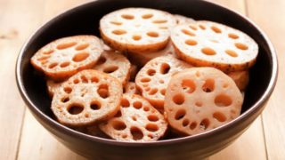 A bowl filled with lotus root chips on a wooden background