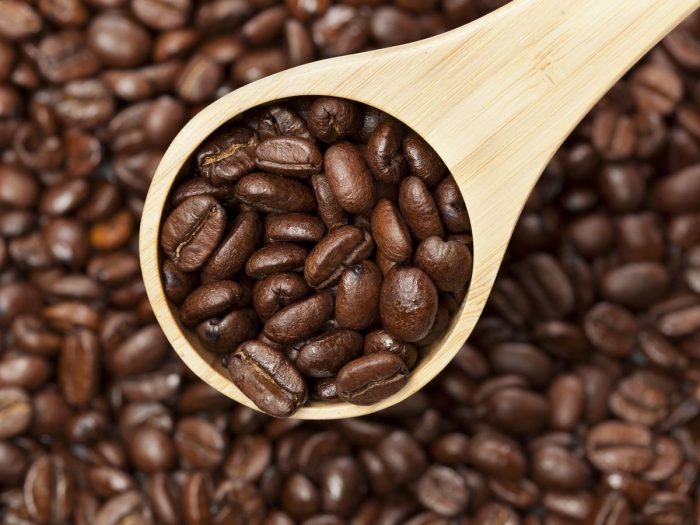 Coffee beans and a wooden spoon filled with the coffee beans
