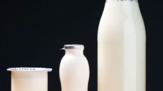 A disposable glass, a small bottle and big bottle of white liquid on a black background.