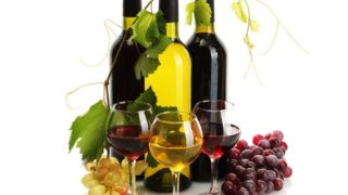 Wineglasses with wine and wine bottles at the back with red and white grapes arranged them.