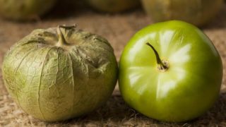 An unripe tomatillo with the ripe tomatillo on a jute cloth