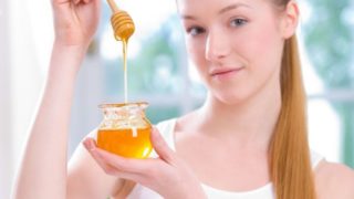 A young beautiful woman holding a small jar of honey