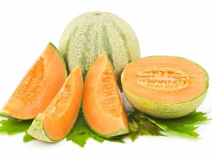 Whole and sliced cantaloupe melons with green leaves on a white background