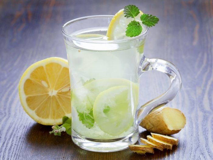 A glass of lemon water with fresh lemon, mint and sliced ginger on a wooden table