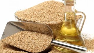 A jar of sesame oil with a steel scoop and bowl filled with sesame seeds