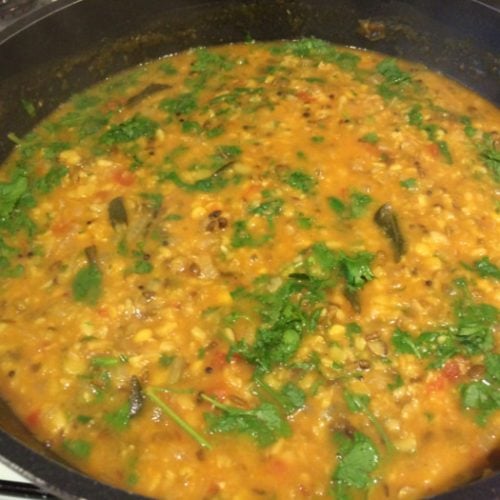 Organic mixed tadka dal in a saucepan, garnished with coriander leaves