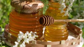 A jar and of acacia honey with a wooden stirrer and white flowers on a wooden tray
