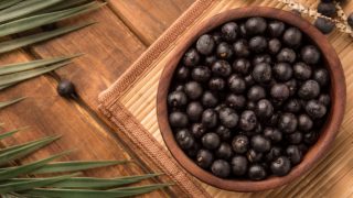 A wooden bowl of fresh acai berries with leaves on a mat