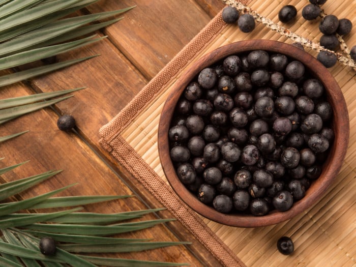 Eine Holzschale mit frischen Acai-Beeren mit Blättern auf einer Matte