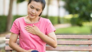 A woman holding her chest while sitting on a bench outdoors