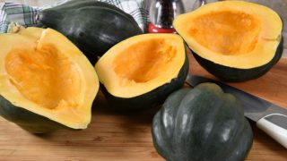 Half sliced acorn squash with a knife on a wooden cutting board