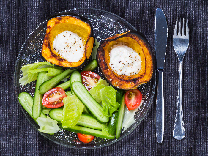 Roasted acorn squash with sour cream and salad, served on a glass plate with a fork and knife on the side