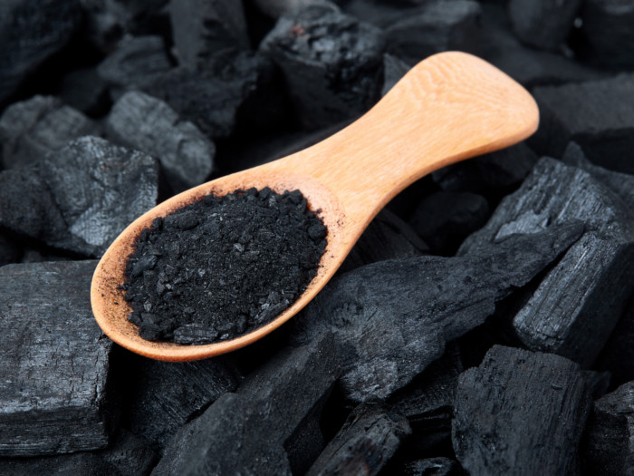 A wooden spoon with activated charcoal powder resting on charcoal pieces