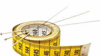 A measuring tape beneath three needles with a white background