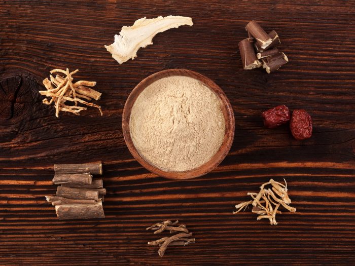 Different varieties of adaptogenic herbs around a bowl of herbal powder