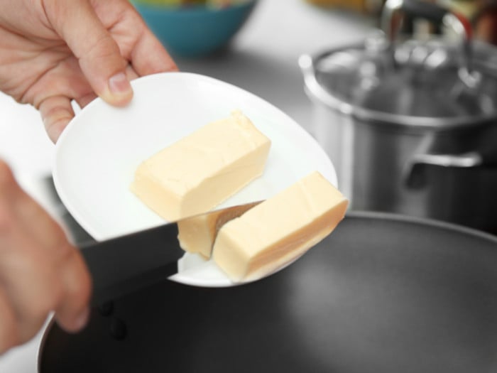 Close-up of someone adding butter to a pan.