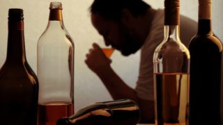 Four half-empty bottles of alcohol with a silhouette of a man drinking in the background