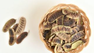 Flatlay picture of a basket of Alexandria senna pods on a white surface.