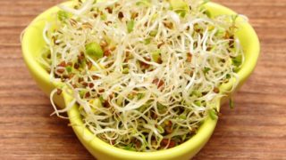 A yellow bowl of alfalfa sprouts on a wooden table