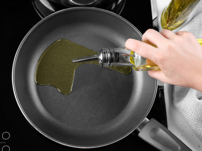 A woman pouring oil from a bottle into a frying pan