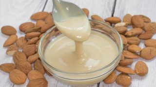 Whole almonds and a bowl of creamy almond butter, with a spoon