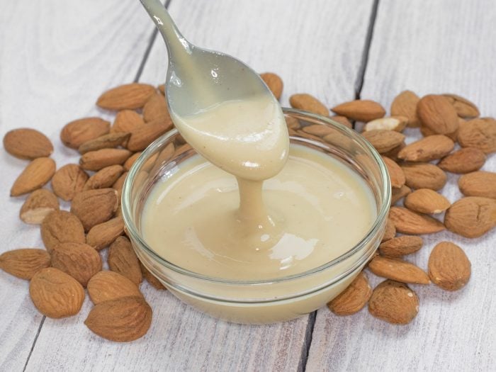 Whole almonds and a bowl of creamy almond butter, with a spoon