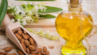 Whole almonds in a rustic spoon, blossoms, and a bottle of almond essential oil