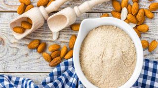 A flat lay picture of a bowl of almond flour kept next to almonds on a wooden table