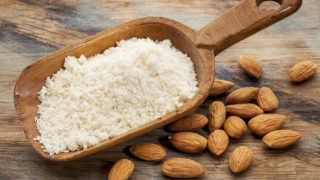 Fresh almond powder in a wooden spoon with loose almonds scattered