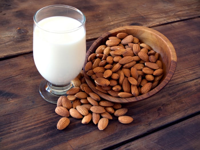 A glass filled with milk and a couple of almonds kept around it