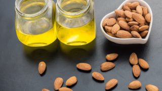Jars of almond oil and a heart-shaped bowl of almonds on a grey table