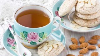 A close-up shot of almond tea served with an almond cookie and placed next to almonds on a table