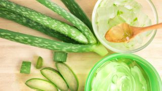 Fresh aloe vera, a bowl of aloe vera gel and a bowl of sliced aloe vera on a wooden table