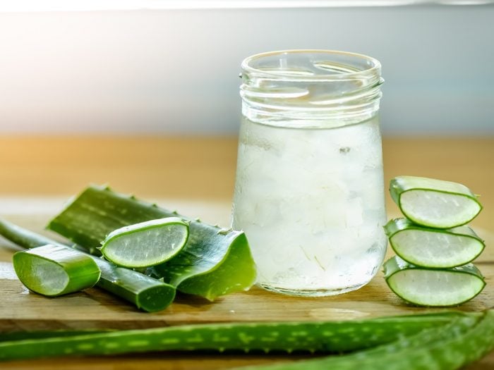 Fresh aloe vera leaves and a glass of aloe vera juice on a wooden table