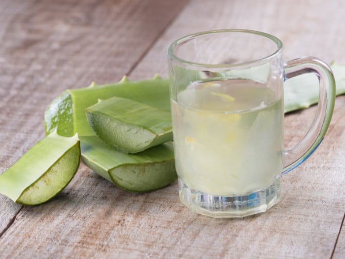A glass filled with aloe vera juice and pieces of aloe vera on a table