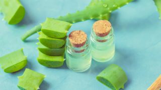 Aloe vera leaf, leaf slices, and two bottles with oil next to it on a blue background