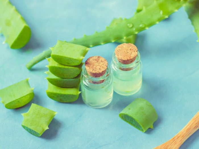 Aloe vera leaf, leaf slices, and two bottles with oil next to it on a blue background