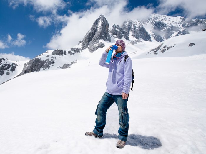 A man standing on a snow covered mountain drinking water