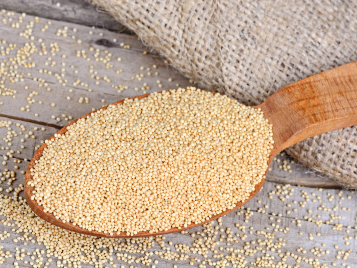 A wooden spoon over filled with amaranth grains on a wooden table