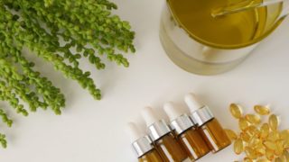Jars of amber oil with capsules and amber plant on a plain surface