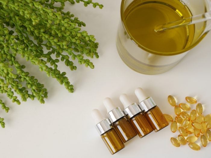 Jars of amber oil with capsules and amber plant on a plain surface
